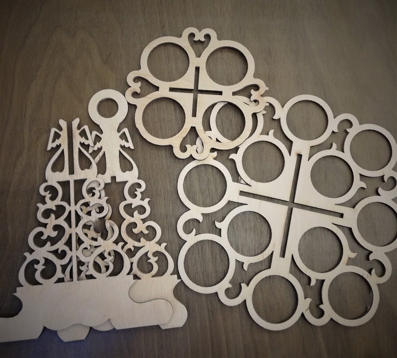 May include: Two wooden cutout designs for holding cups or glasses. The larger design has eight circular cutouts and the smaller design has six circular cutouts. Both designs have intricate patterns.