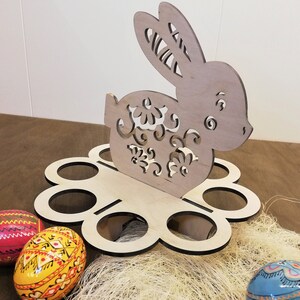 May include: Wooden Easter egg holder shaped like a bunny with intricate cutouts. The holder has six egg slots and is decorated with a floral pattern.