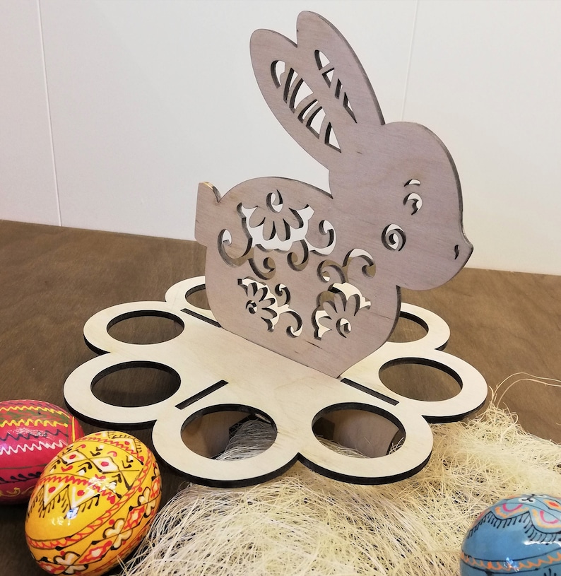 May include: Wooden Easter egg holder shaped like a bunny with intricate cutouts. The holder has six egg slots and is decorated with a floral pattern.