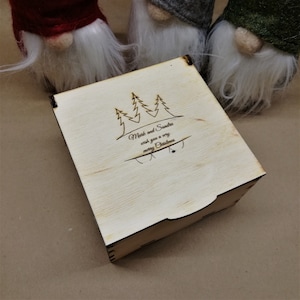 May include: A wooden box with a hinged lid. The box is decorated with a laser-engraved design of three pine trees and the text "Mark and Sandra wish you a very merry Christmas".