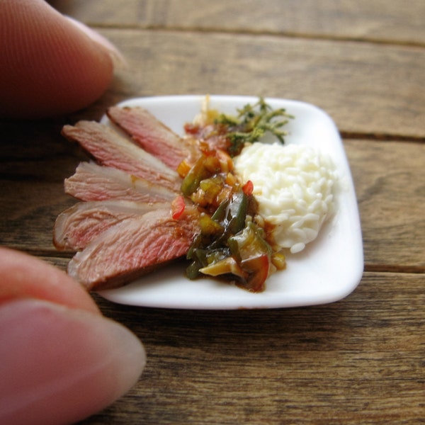 Asian style sliced duck breast, rice and stir-fried vegetables on a square plate