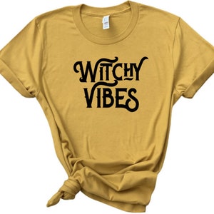 K&ouml;nnte beinhalten: Ein senfgelbes T-Shirt mit schwarzem Text, der "Witchy Vibes" lautet.