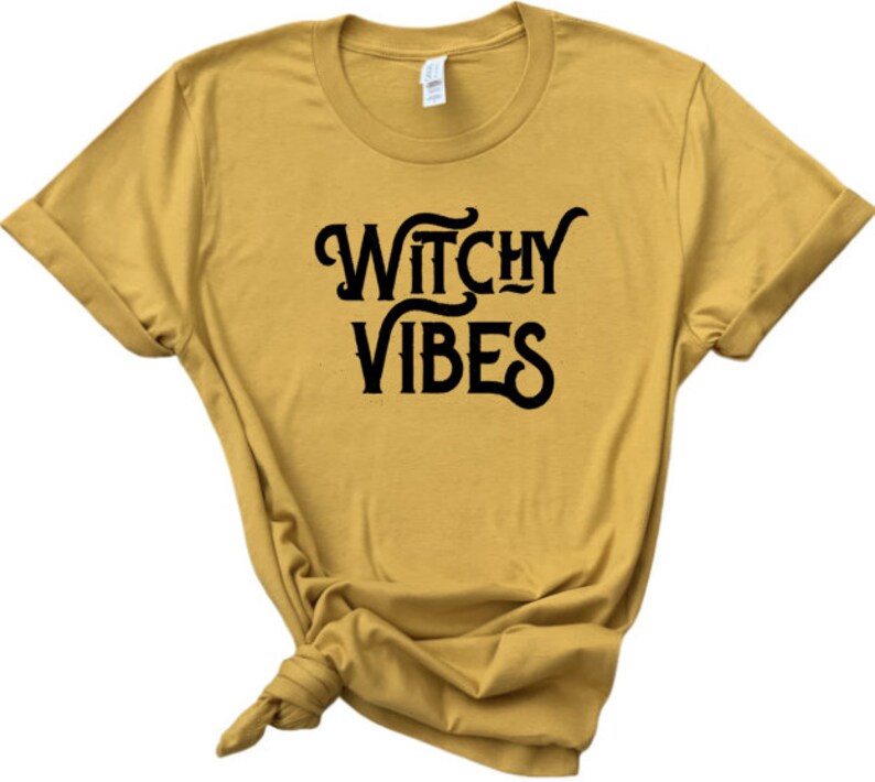 K&ouml;nnte beinhalten: Ein senfgelbes T-Shirt mit schwarzem Text, der "Witchy Vibes" lautet.