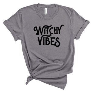 K&ouml;nnte beinhalten: Ein heidefarbenes T-Shirt mit dem Aufdruck "Witchy Vibes" in Schwarz.