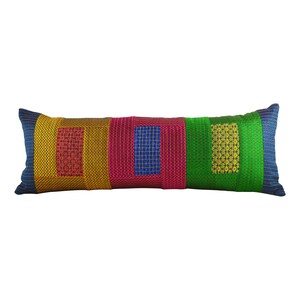 May include: A long rectangular pillow with a patchwork design. The pillow is made of four different colored fabrics: yellow, pink, blue, and green. Each fabric has a different pattern.