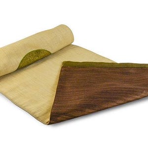 May include: A beige table runner with a green and brown design. The runner is rolled up and has a brown and gold trim.