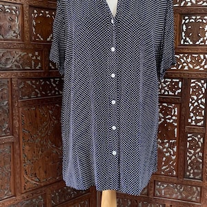 May include: A navy blue short-sleeved button-down shirt featuring a white polka dot pattern. The shirt has a classic collar, a front button placket with white buttons, and a relaxed fit, displayed on a beige mannequin torso.