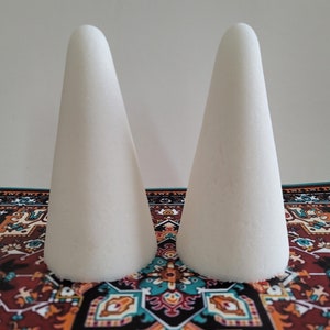 May include: Two white foam cones on a colorful patterned rug. The cones are smooth and have a pointed top.