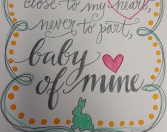Puede incluir: Una ilustración dibujada a mano con un borde verde y amarillo. La ilustración presenta un corazón y conejos con el texto "Rest your head close to my heart, never to part, baby of mine".