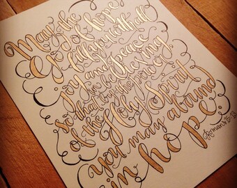 Puede incluir: Una pieza de caligrafía manuscrita con tinta dorada sobre un fondo beige. El texto dice "Que la alegría y la paz del Espíritu Santo abunden en vosotros en esperanza." El texto está en una fuente cursiva y está rodeado de adornos decorativos. El texto es de Romanos 15:13.