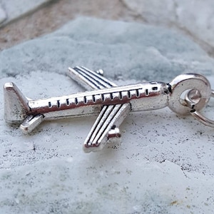 Peut inclure: Breloque d'avion en argent avec une boucle pour l'attacher à un collier ou un bracelet. Le charme est détaillé avec un corps et des ailes texturés.