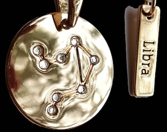 May include: Gold-tone pendant necklace featuring the Libra zodiac constellation with clear crystal accents. The pendant is attached to a gold-tone chain with a lobster clasp. The necklace comes with a separate gold-tone tag that reads "Libra".