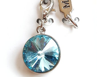 May include: A silver charm featuring a round, light blue crystal pendant with multiple facets. The charm has a lobster clasp and a small tag with the word "March". The crystal is set in a silver bezel.