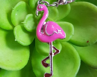 May include: Pink flamingo charm with a silver metal body and a silver clip. The charm is on a green background.