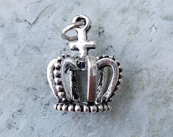 Puede incluir: Encanto de plata en forma de corona con una cruz en la parte superior. La corona tiene un diseño detallado con pequeñas cuentas alrededor de los bordes.
