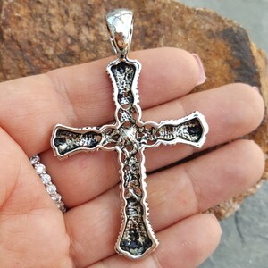 May include: A silver cross pendant with intricate detailing. The cross is made of sterling silver and has a detailed design.