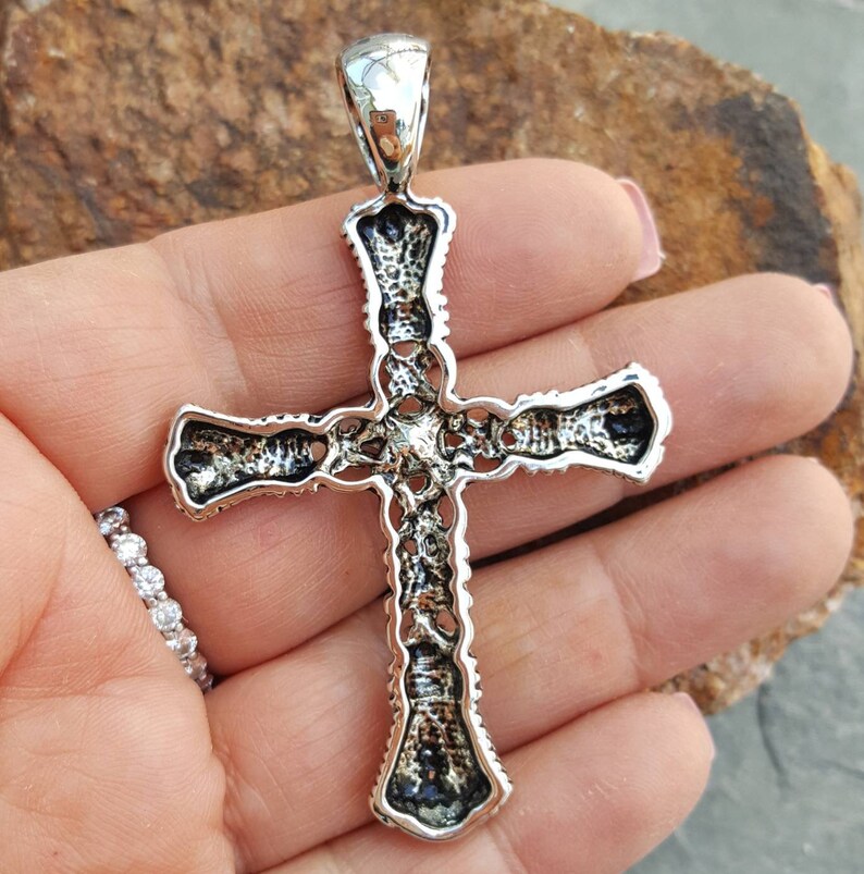 May include: A silver cross pendant with intricate detailing. The cross is made of sterling silver and has a detailed design.