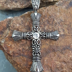 May include: A silver cross pendant with an ornate design and a clear rhinestone in the centre.