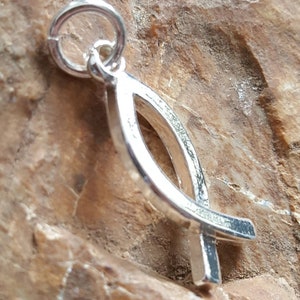 May include: Silver charm in the shape of a stylized fish with a cross at the bottom. The charm has a loop at the top for attaching to a necklace or bracelet.