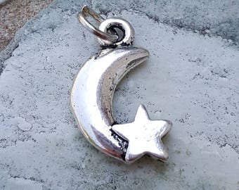 May include: A silver charm in the shape of a crescent moon with a five-pointed star. The charm is designed to be used on a necklace or bracelet.
