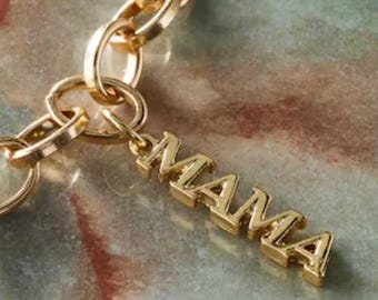 May include: A gold-colored chain necklace with a pendant that spells out the word "MAMA". The pendant is in a block letter style. The chain links are large and round.