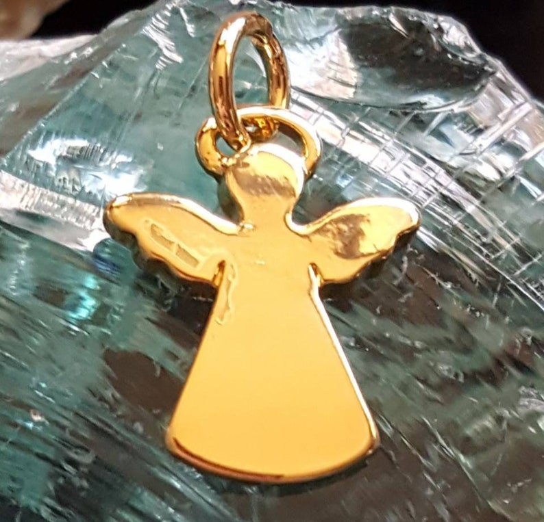 May include: A gold angel charm pendant with a halo and wings. The charm is on a green background.
