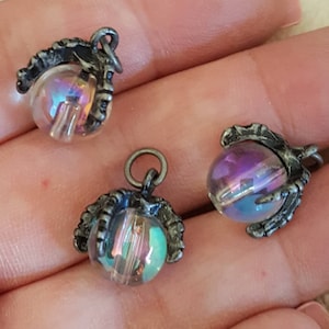 Puede incluir: Tres abalorios de garra plateados con orbes de vidrio iridiscente. Cada abalorio tiene un bucle para sujetarlo a un collar o pulsera.