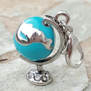 May include: A silver charm in the shape of a globe with a turquoise blue globe and silver continents. The globe is on a silver stand with a silver clasp.