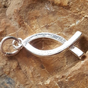 May include: Silver charm in the shape of a stylized fish, a Christian symbol. The charm has a loop for attaching to a necklace or bracelet.