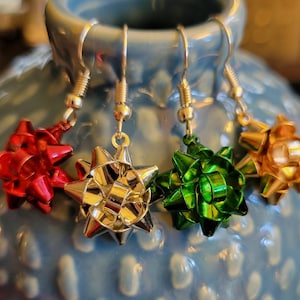 May include: Four pairs of silver bow earrings. The bows are made of shiny metallic paper in red, silver, green, and gold.