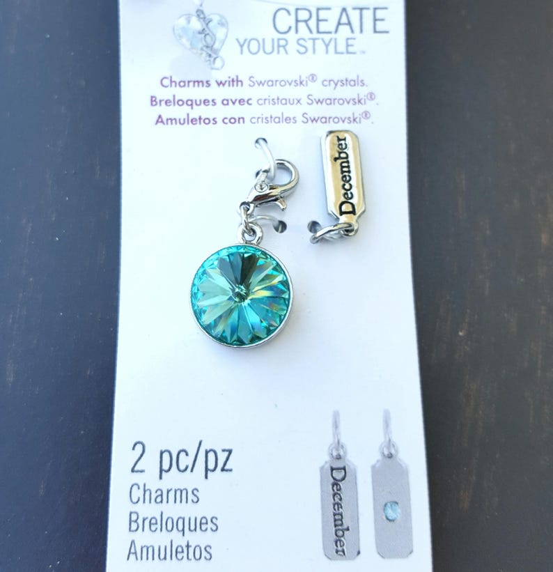 May include: A turquoise blue crystal charm with a silver clasp and a silver tag that says "December". The charm is packaged on a white card with the words "Create Your Style" and "Charms with Swarovski crystals".