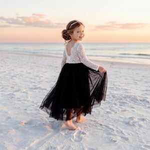 May include: A long-sleeved dress featuring a white lace bodice with a scoop neckline and a full-length black tulle skirt. The garment has a fitted lace top that transitions into a voluminous, layered black skirt that reaches the ankles.