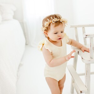 Puede incluir: Una ni&ntilde;a peque&ntilde;a con un mono blanco y amarillo con volantes y una diadema dorada con cuentas blancas. La ni&ntilde;a est&aacute; de pie junto a una silla de madera blanca.