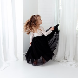 May include: A dress featuring a white long-sleeved lace bodice with a scoop neckline and a floor-length black tulle skirt. The garment has a fitted waistline where the intricate white lace meets the voluminous, layered black tulle fabric.