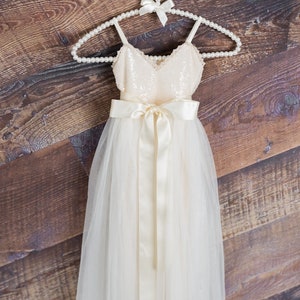 May include: A white tulle dress with a sequined bodice and a satin sash. The dress is hanging on a pearl-beaded hanger.