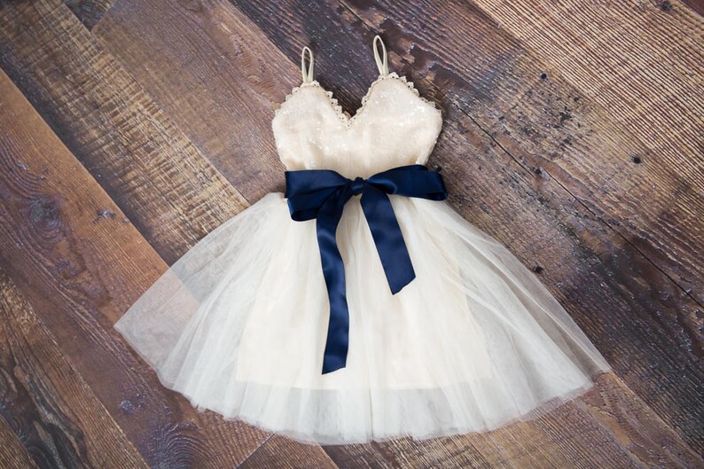 May include: A white tulle dress with a sequined bodice and a navy blue satin ribbon tied in a bow at the waist.
