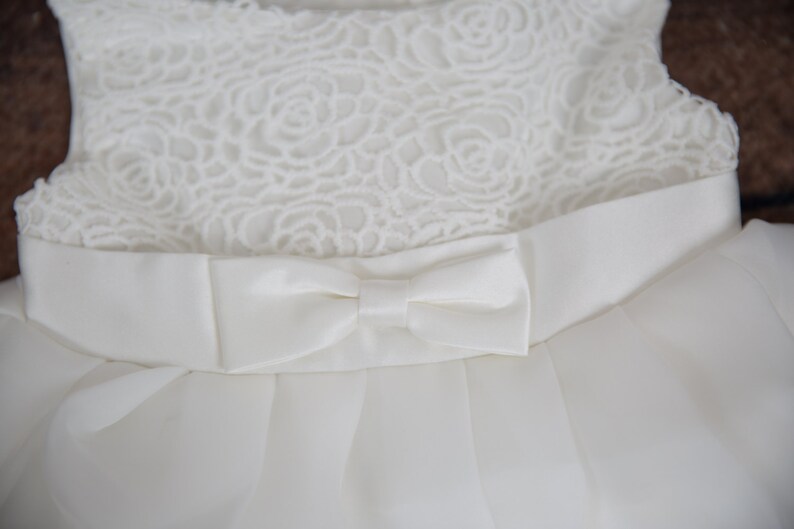 Puede incluir: Un vestido blanco sin mangas con un corpi&ntilde;o de encaje y un lazo de sat&eacute;n en la cintura.