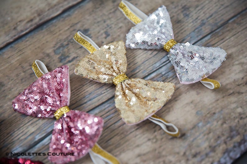 May include: Three sequined bow headbands in pink, gold, and silver with gold elastic bands.