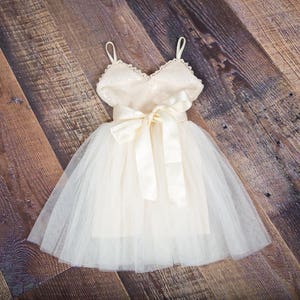 May include: A white tulle dress with a sequined bodice and a satin sash. The dress has a fitted bodice and a full skirt.