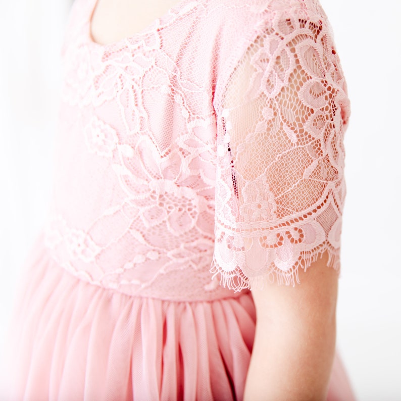 Pode incluir: Um vestido de tule rosa com um corpete de renda e mangas curtas. O vestido tem uma renda festonada.