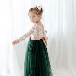 Pu&ograve; includere: Un abito lungo fino ai piedi con corpetto in pizzo bianco a maniche lunghe e profonda scollatura sulla schiena. La gonna &egrave; in tulle verde scuro, impreziosita in vita da un ampio nastro di raso color marrone chiaro annodato sul retro.