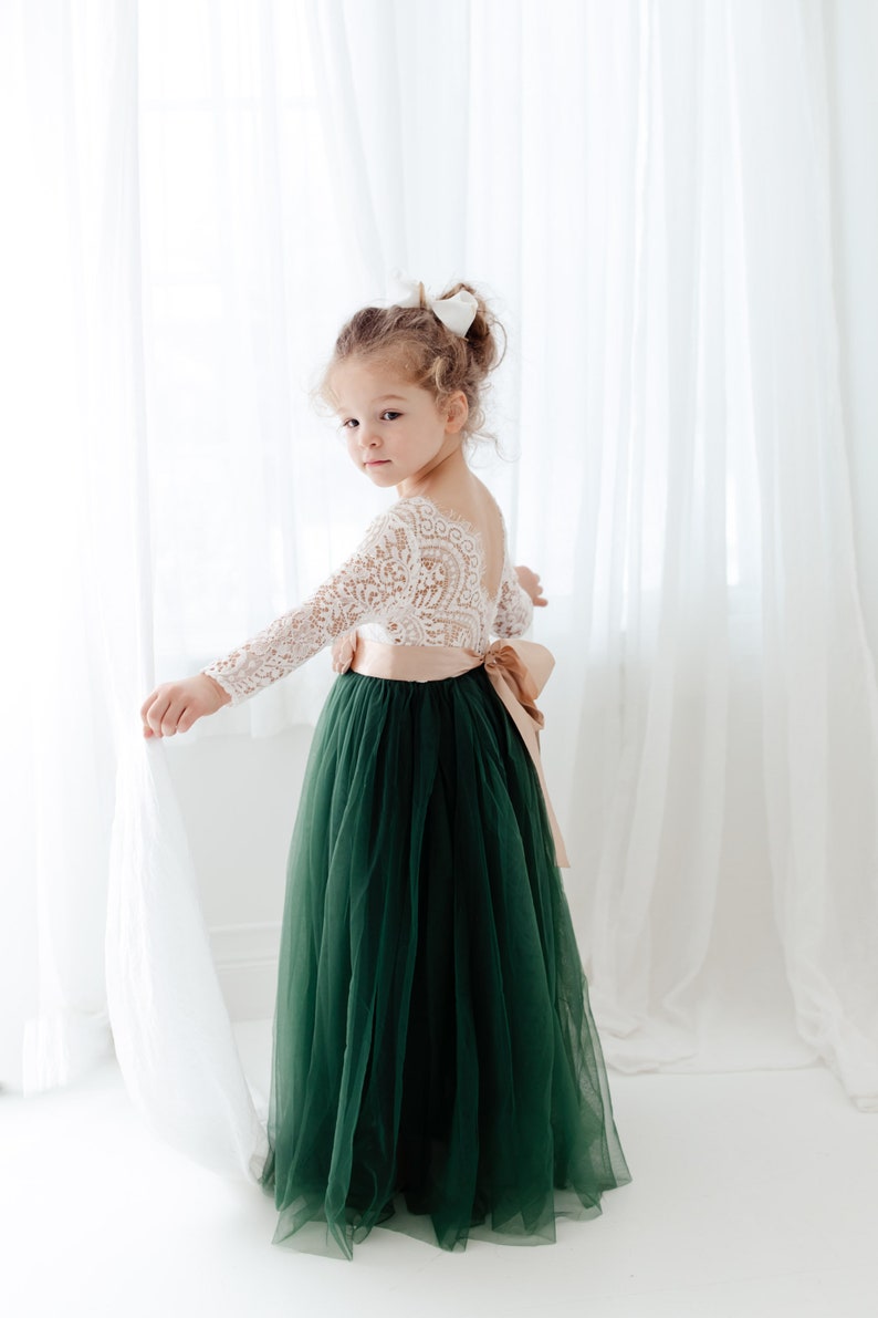 Pu&ograve; includere: Un abito lungo fino ai piedi con corpetto in pizzo bianco a maniche lunghe e profonda scollatura sulla schiena. La gonna &egrave; in tulle verde scuro, impreziosita in vita da un ampio nastro di raso color marrone chiaro annodato sul retro.
