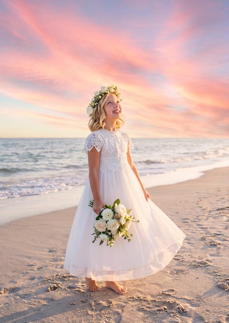 May include: A white floor-length dress with short lace sleeves and a lace bodice overlay. The dress features a full tulle skirt and is paired with a floral crown of white roses and greenery, along with a matching bouquet of white roses and foliage.