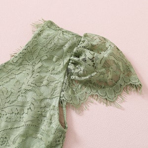 K&ouml;nnte beinhalten: Nahaufnahme eines gr&uuml;nen Spitzenstoffes mit einem gewellten Rand. Der Stoff hat ein zartes Blumenmuster und eine weiche, flie&szlig;ende Textur.