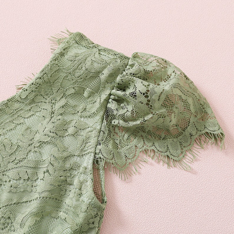 K&ouml;nnte beinhalten: Nahaufnahme eines gr&uuml;nen Spitzenstoffes mit einem gewellten Rand. Der Stoff hat ein zartes Blumenmuster und eine weiche, flie&szlig;ende Textur.