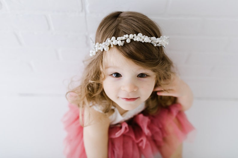 May include: A young girl with long brown hair wearing a pink tulle dress and a pearl and crystal headband.