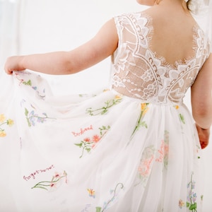 Puede incluir: Vestido blanco de tul con bordado floral y las palabras "no me olvides" y "semillas de p&aacute;jaro" bordadas en la falda. El vestido tiene una espalda de encaje.