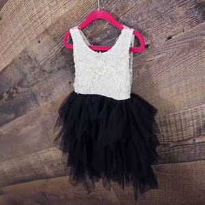 Puede incluir: Un vestido de tul blanco y negro con falda de volantes colgado de una percha rosa sobre un fondo de madera.