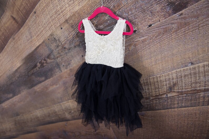 Puede incluir: Un vestido de tul blanco y negro con falda de volantes colgado de una percha rosa sobre un fondo de madera.