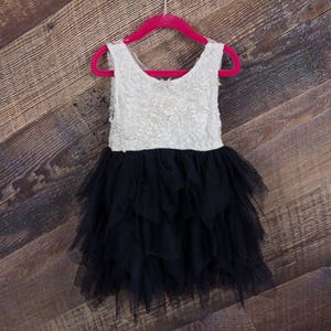 Puede incluir: Un vestido de tul blanco y negro con un corpi&ntilde;o de encaje. El vestido est&aacute; colgado en una percha roja contra un fondo de madera.